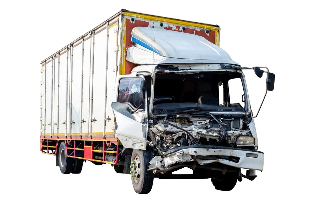 A full-body view of the front and side of a big truck damaged in an accident on the road.