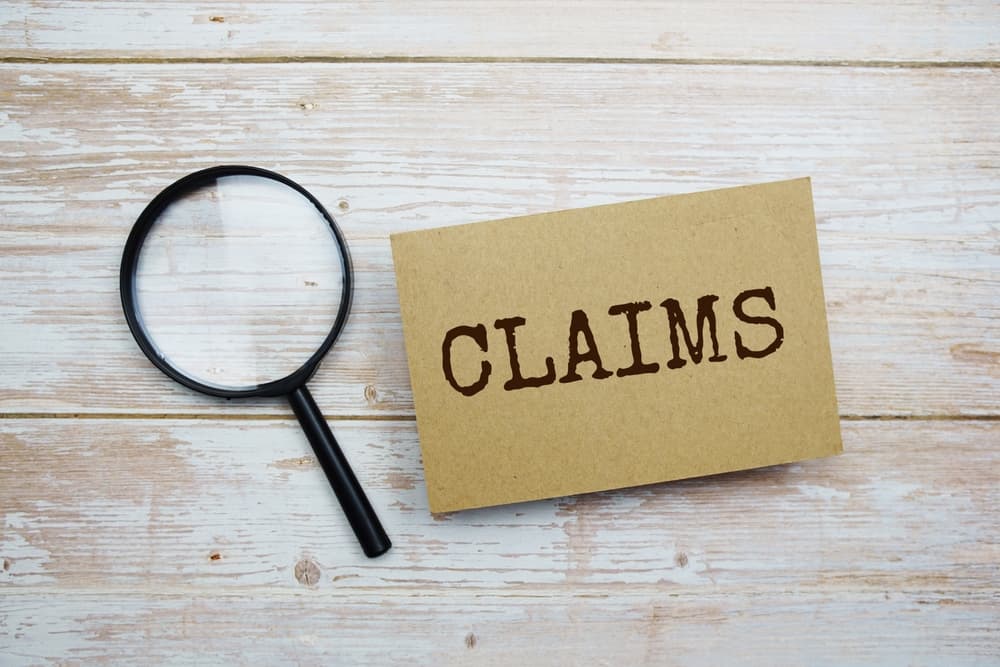 Claims written on card and magnifying glass on wooden background